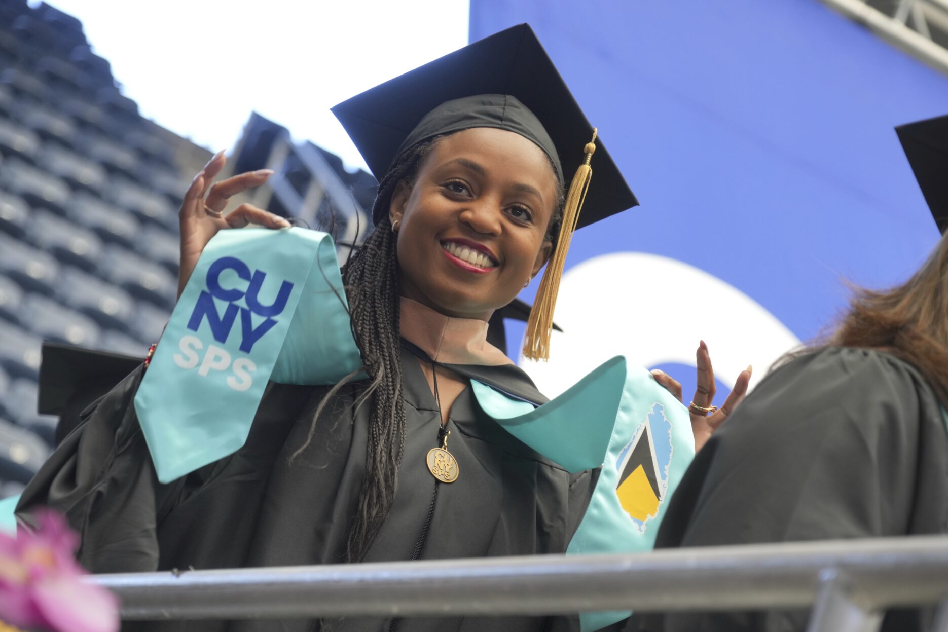 A CUNY SPS grad holding up her sash during the 2023 commencement in Louis Armstrong Stadium in Queens.