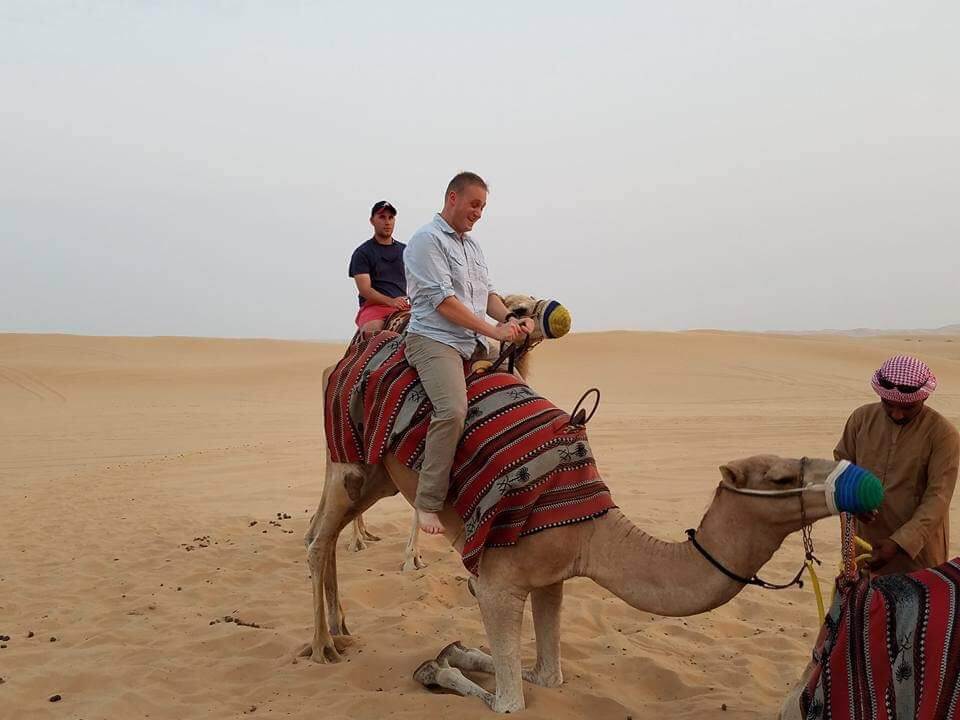 A photo of CUNY SPS student Lt. Julian Stuart riding a camel in the desert.