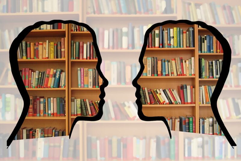 A stock image of a library with two silhouetted heads facing each other superimposed over the bookshelves.